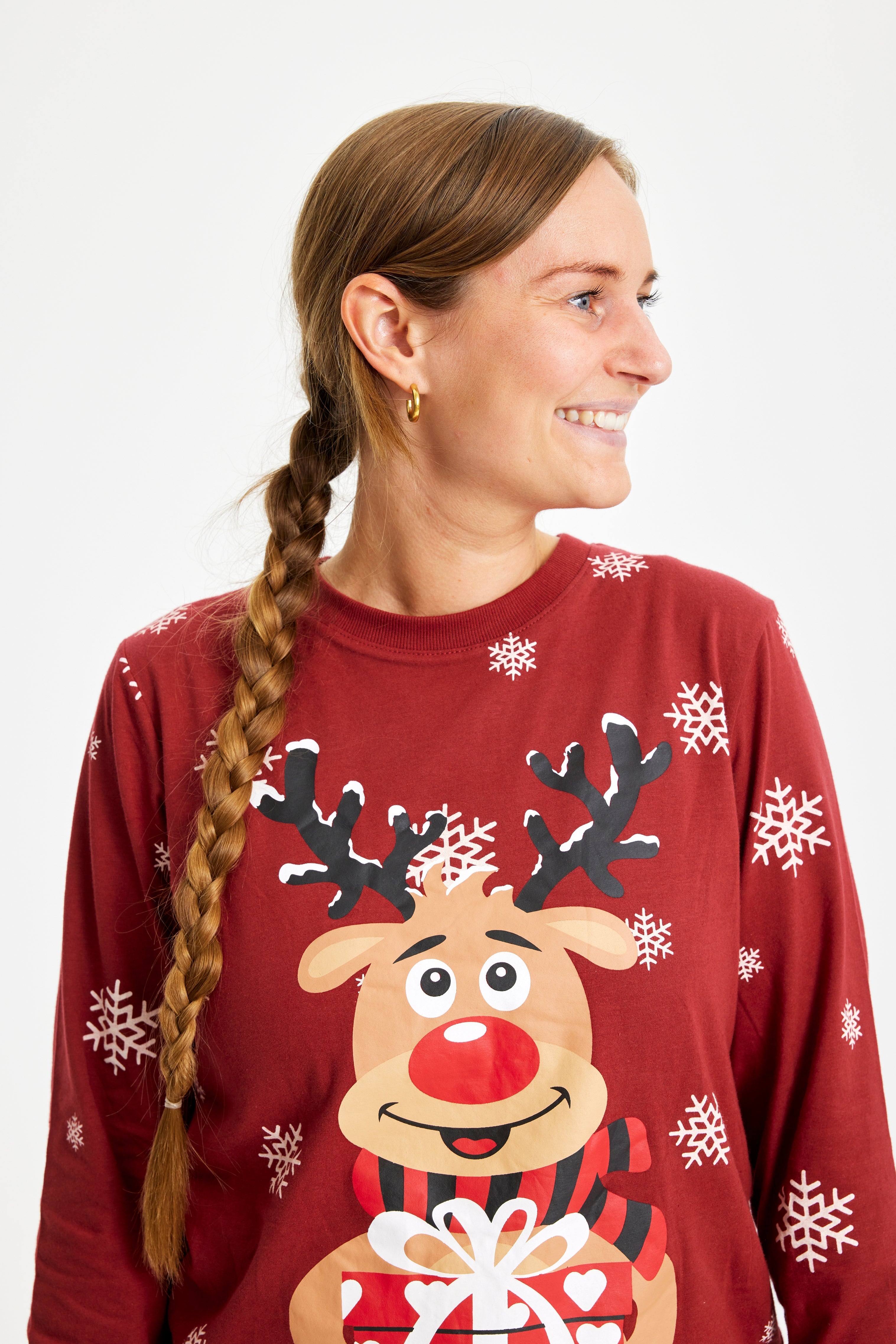 En smilende kvinne i rød julepyjamas med reinsdyr og snøfnugg.